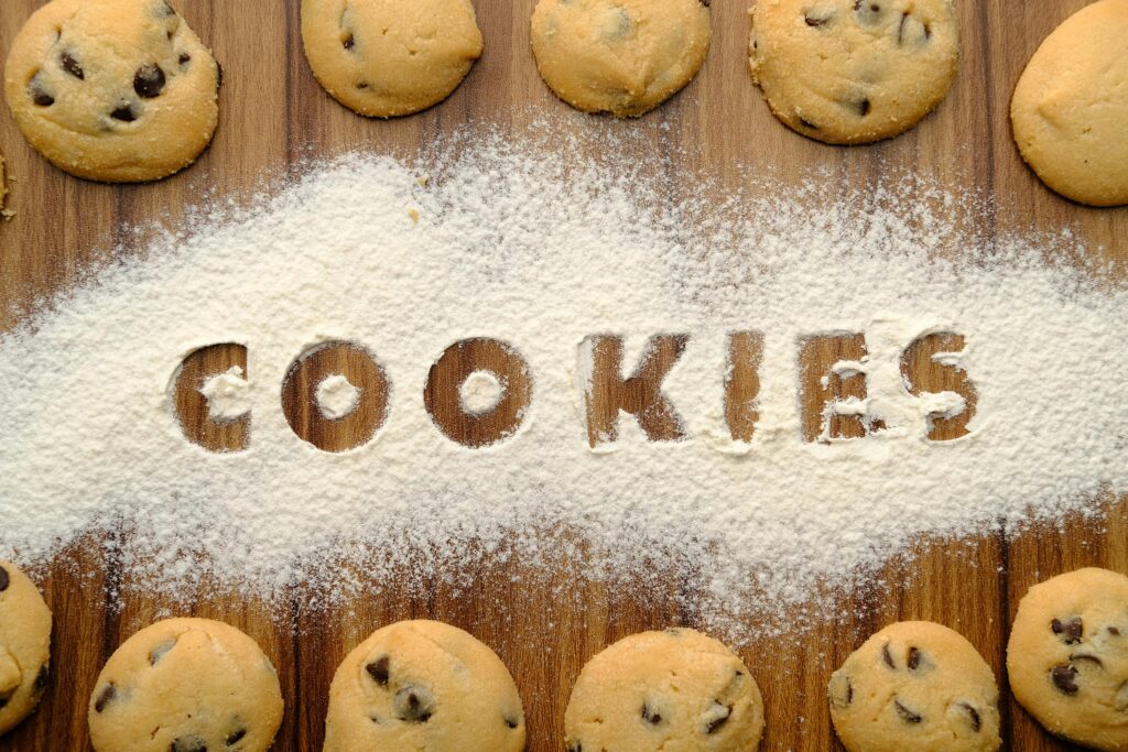 Freshly baked chocolate chip cookies arranged on flour-dusted wooden table.